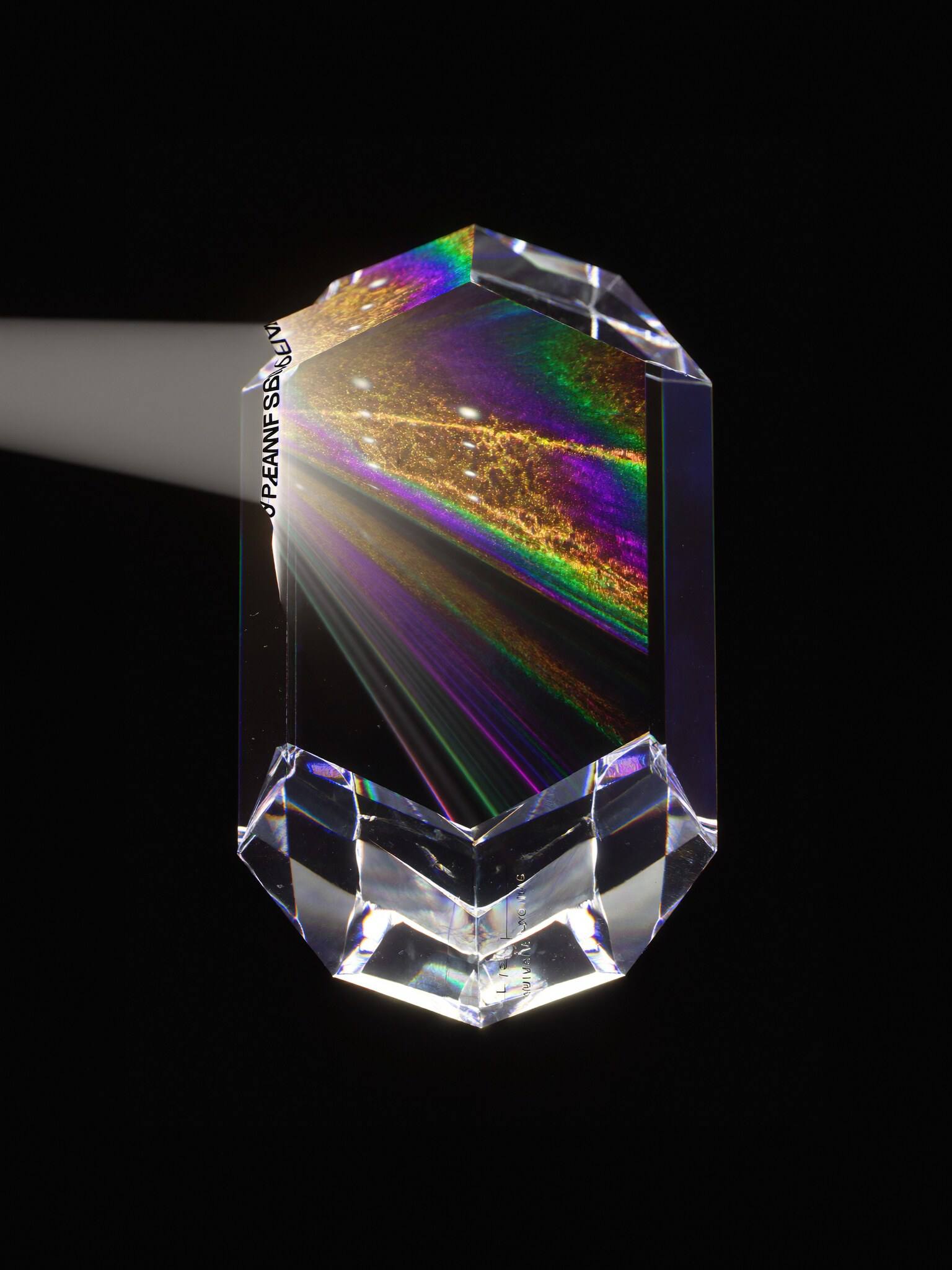 A faceted glass prism splitting light into violet and gold rays